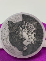 Load image into Gallery viewer, Close-up of Jaguar and black jaguar etched on a polished selenite charging plate that can be used for charging crystals &amp; jewelry. Selenite ranges from translucent to milky white in color. The etched jaguar is the head only and half of it is a black Jaguar on a white background and the other half is a white, spotted jaguar on a black background. Average weight is 9.1 oz., and average size is approx. 4&quot; in diameter and approx. ½&quot; thick. This selenite is ethically sourced and workers are paid living wages.
