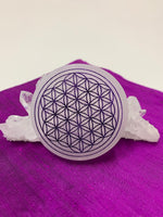 Load image into Gallery viewer, Flower of life etched on smooth, white, 3&quot; selenite plate/disk. The selenite ranges from Translucent to milky white in color.  This plate can be used for charging your crystals and jewelry. The etched flower of life, painted, purple on this plate symbolizes (among other things)  unity of all things, creation and the Universe. Weight and size varies, but average weight is 4.9 oz, size is approximately 3&quot; in diameter and about ½&quot; thick. The selenite is ethically sourced and workers receive living wages.
