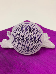 Flower of life etched on smooth, white, 3" selenite plate/disk. The selenite ranges from Translucent to milky white in color.  This plate can be used for charging your crystals and jewelry. The etched flower of life, painted, purple on this plate symbolizes (among other things)  unity of all things, creation and the Universe. Weight and size varies, but average weight is 4.9 oz, size is approximately 3" in diameter and about ½" thick. The selenite is ethically sourced and workers receive living wages.