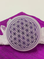 Load image into Gallery viewer, Close-up view. Flower of life etched on smooth, white, 3&quot; selenite plate/disk. The selenite ranges from Translucent to milky white in color. This plate can be used for charging your crystals and jewelry. The etched flower of life, painted, purple on this plate symbolizes (among other things) unity of all things, creation and the Universe. Average weight is 4.9 oz, size is approximately 3&quot; in diameter and about ½&quot; thick. The selenite is ethically sourced and workers receive living wages.
