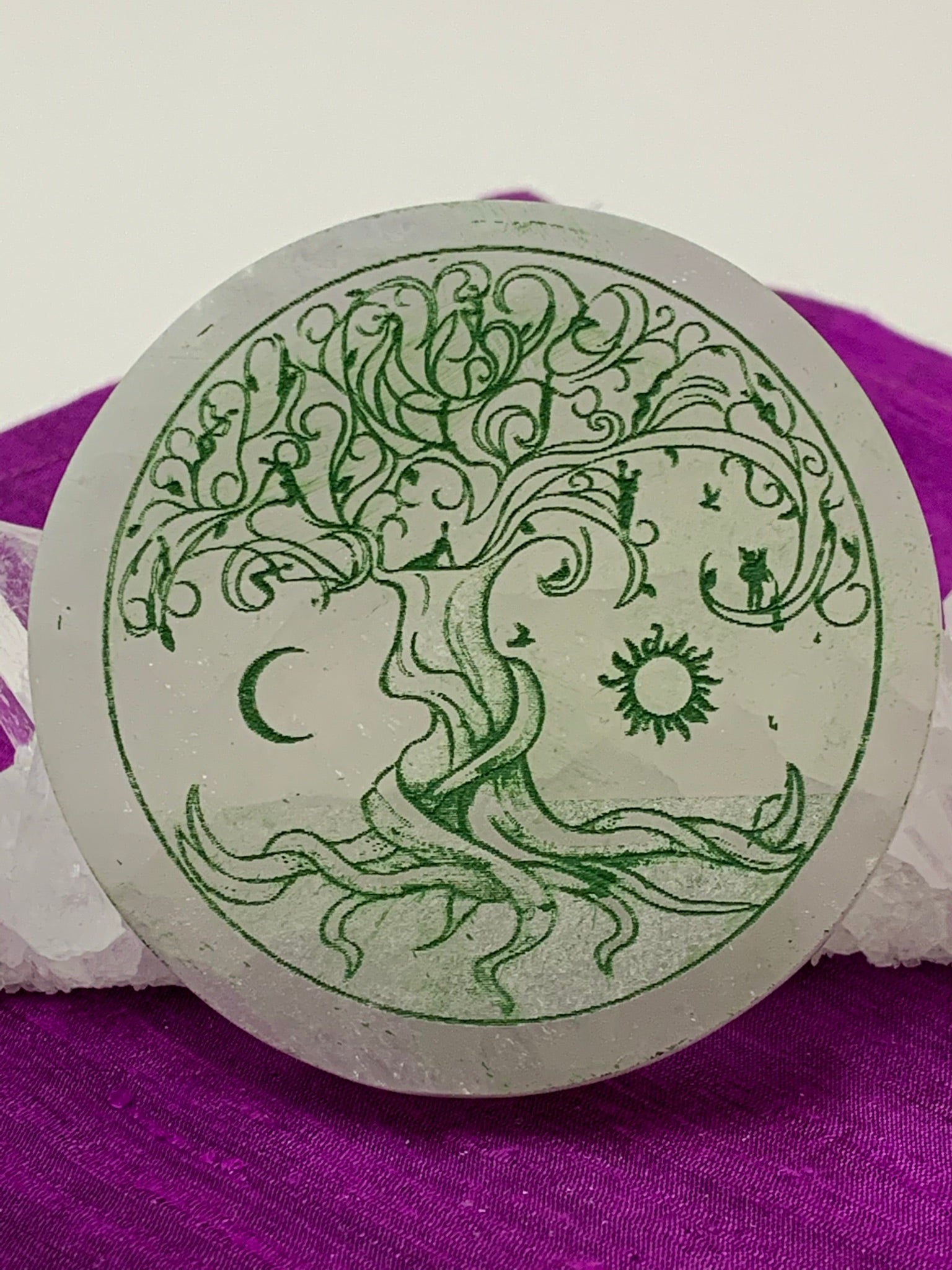 Close-up view of the Celtic Tree of Life etched on smooth, white selenite plate, used for charging your crystals and jewelry (or just for décor). The etched tree is painted green and the selenite plate ranges from translucent to milky white in color. Weight & size vary, but average weight is 4.9 oz, size is approximately 3" in diameter and approximately ½" thick. The selenite is ethically sourced and workers are paid living wages.