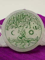 Load image into Gallery viewer, Close-up view of the Celtic Tree of Life etched on smooth, white selenite plate, used for charging your crystals and jewelry (or just for décor). The etched tree is painted green and the selenite plate ranges from translucent to milky white in color. Weight &amp; size vary, but average weight is 4.9 oz, size is approximately 3&quot; in diameter and approximately ½&quot; thick. The selenite is ethically sourced and workers are paid living wages.
