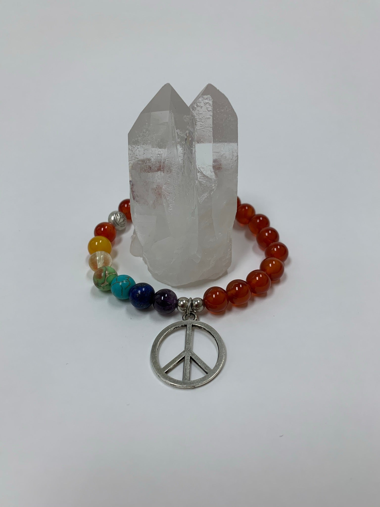 Carnelian gemstone power bracelet, accented by 7 different gemstones, representing the 7 chakras and a silver-colored peace sign charm and 3 additional silver-colored beads (2 of which are plain and one has a lotus on it). These additional silver colored beads are not sterling silver. 