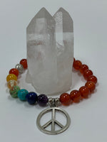 Load image into Gallery viewer, Close-up of the carnelian gemstone power bracelet, accented by 7 different gemstones, representing the 7 chakras and a silver-colored peace sign charm and 3 additional silver-colored beads (2 of which are plain and one has a lotus on it). These additional silver colored beads are not sterling silver.
