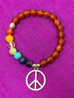 Load image into Gallery viewer, Second Close-up of the carnelian gemstone power bracelet, accented by 7 different gemstones, representing the 7 chakras and a silver-colored peace sign charm and 3 additional silver-colored beads (2 of which are plain and one has a lotus on it). These additional silver colored beads are not sterling silver.
