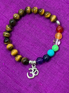 Second close-up view. Tiger eye power bracelet, accented with 7 additional gemstone beads, one to represent each of the 7 chakras, a silver colored "Om" charm and 3 additional silver colored beads (2 plain and one with a lotus on it). Silver colored beads and charm are not sterling silver. All gemstone beads are 8mm.