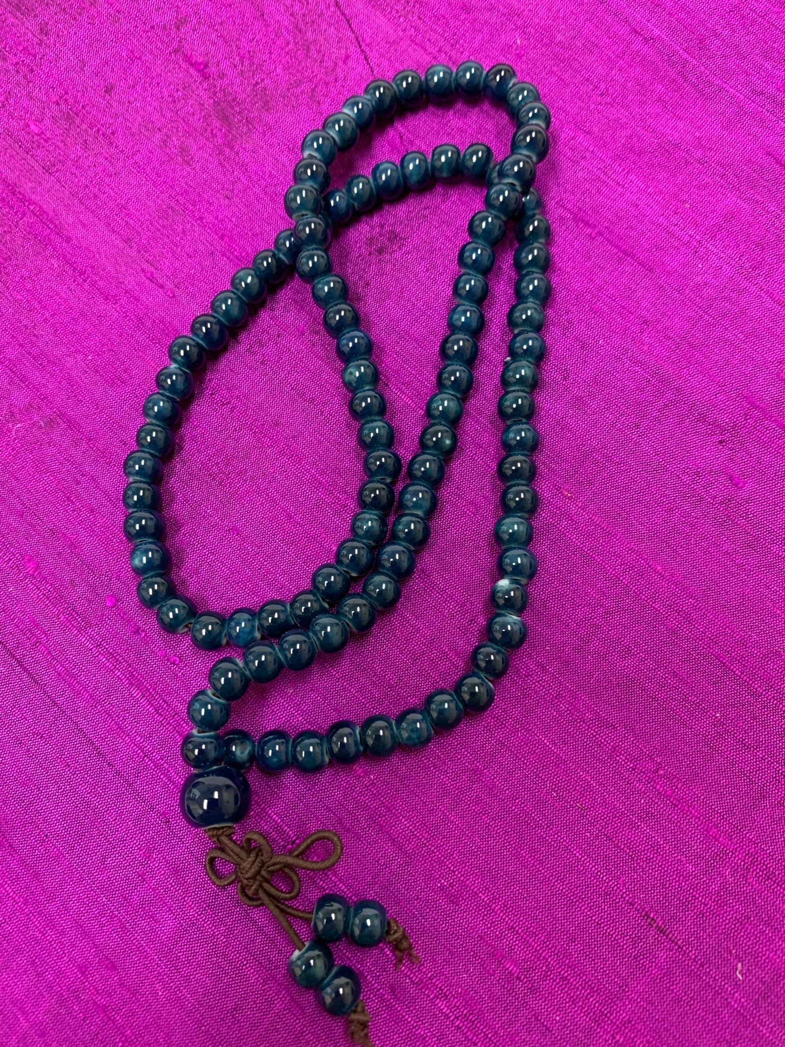 Close-up view. Prayer beads/mala necklace consists of 108 small, blue ceramic beads. Used to count 108 repetitions of a mantra, so the user can pay attention to the sounds, vibrations and meaning of the mantra being chanted.