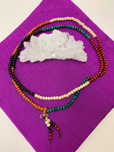Prayer beads/mala necklace strung with 216 beads allowing you to do 2 repetitions of the traditional 108 for chanting mantras during meditation. Beads are all wooden and in a colorful array on the necklace (green, black, tan, orange and brown beads). Twelve of the beads dangle from the necklace in two short, separate strands with a small silver colored accent above them.  Silver colored accent is not sterling silver.