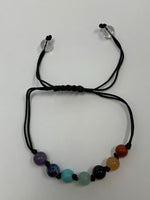 Load image into Gallery viewer, Close-up view. Adjustable Chakra power bracelet consists of 7 stones, one representing each of the 7 major chakras. It is artfully strung together with a strong, thin black cord and a tiny black knot between each chakra stone. Two additional clear quartz crystal stones embellish the adjustable part of the bracelet.
