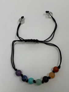 Close-up view. Adjustable Chakra power bracelet consists of 7 stones, one representing each of the 7 major chakras. It is artfully strung together with a strong, thin black cord and a tiny black knot between each chakra stone. Two additional clear quartz crystal stones embellish the adjustable part of the bracelet.