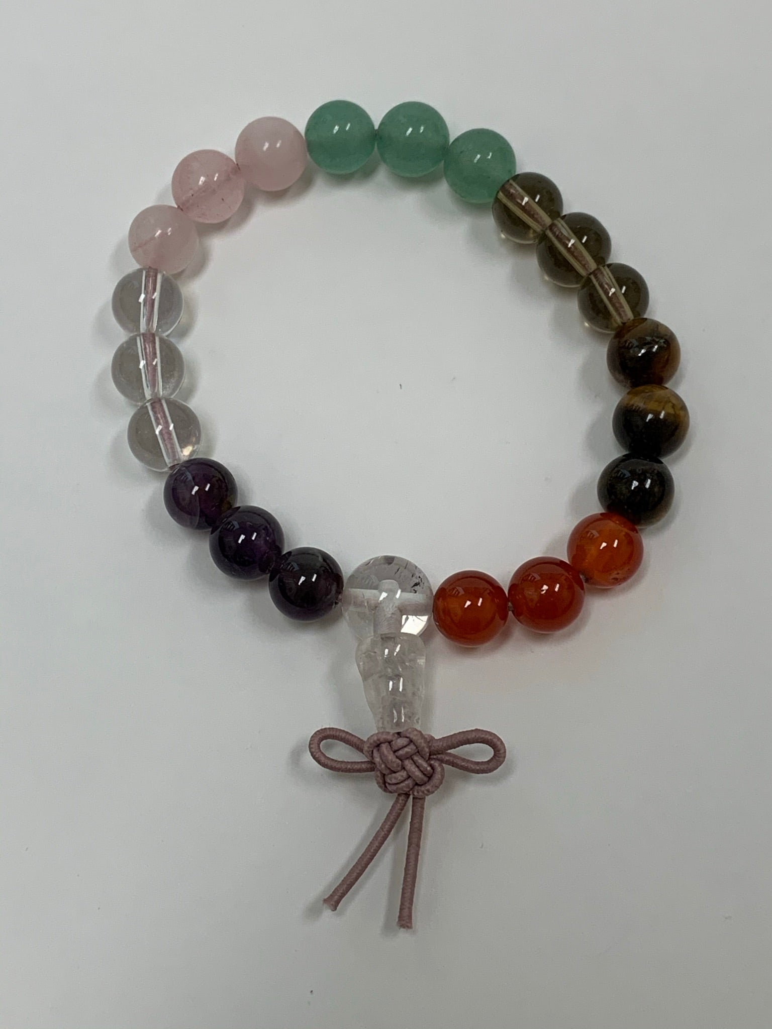Close-up view. Mixed gemstone power bracelet with 7 different gemstones: amethyst, clear quartz, rose quartz, smoky quartz, tiger eye, carnelian, and aventurine. The bracelet is accented by a Chinese tassel knot.