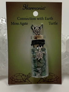 Close-up view. Small corked gemstone chip bottle necklace with moss agate gemstone chips inside, accented with a silver-colored turtle and fancy jewelry bail on the outside. Comes with a thin suede cord to wear as necklace.
