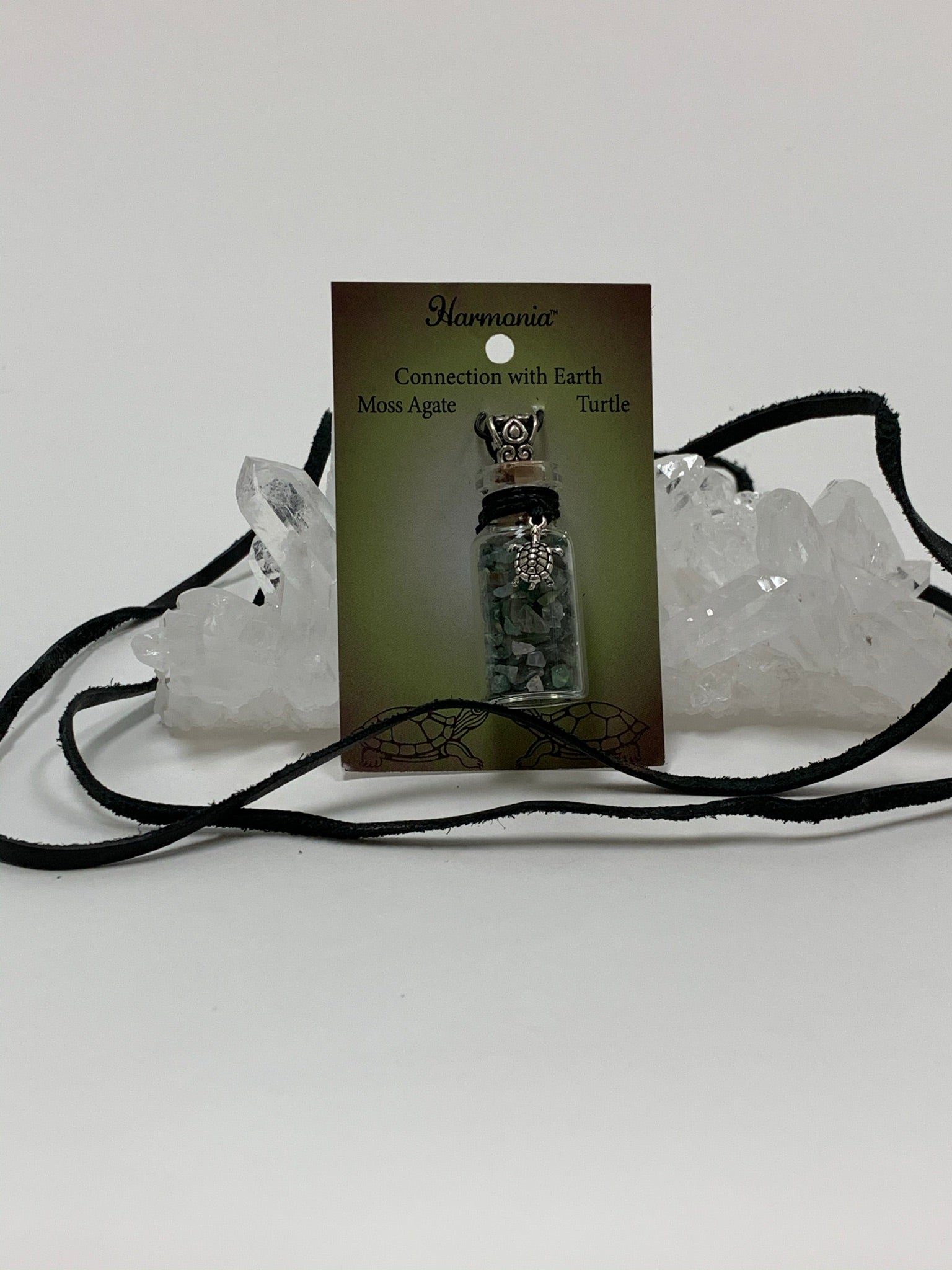View with suede necklace displayed. Small corked gemstone chip bottle necklace with moss agate gemstone chips inside, accented with a silver-colored turtle and fancy jewelry bail on the outside. Comes with a thin suede cord to wear as necklace.
