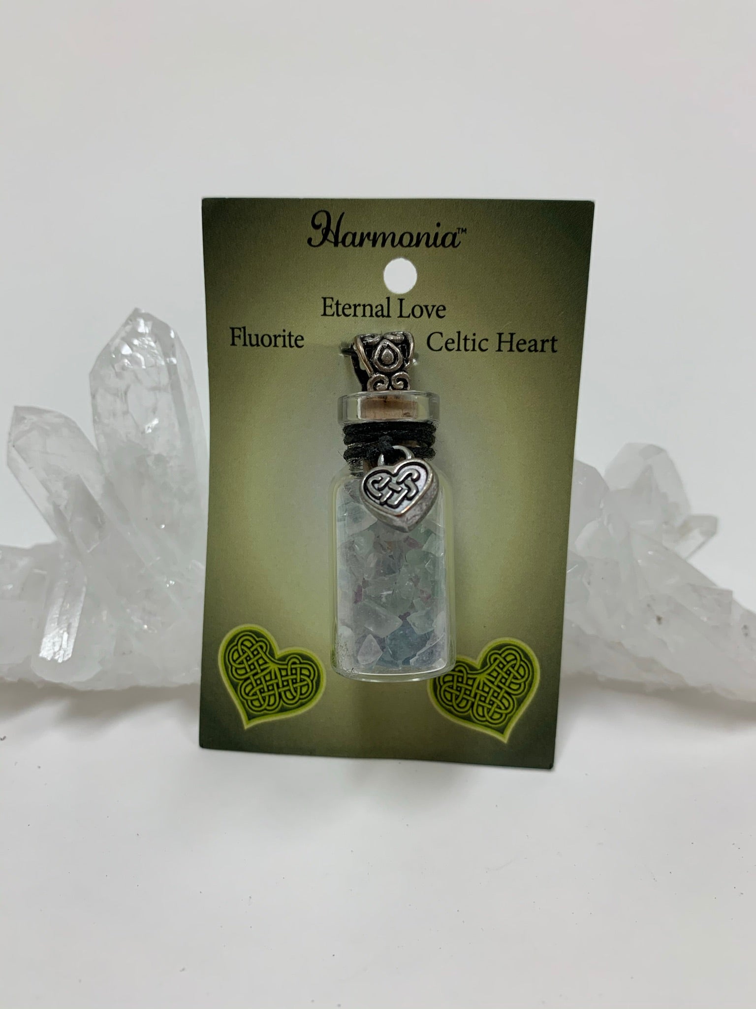 Close-up view of the gemstone chip (corked) bottle necklace with little fluorite chips inside and accented on the outside with a silver-colored Celtic heart and a fancy jewelry bail. It comes with a thin black suede cord so the bottle can be worn as a necklace.