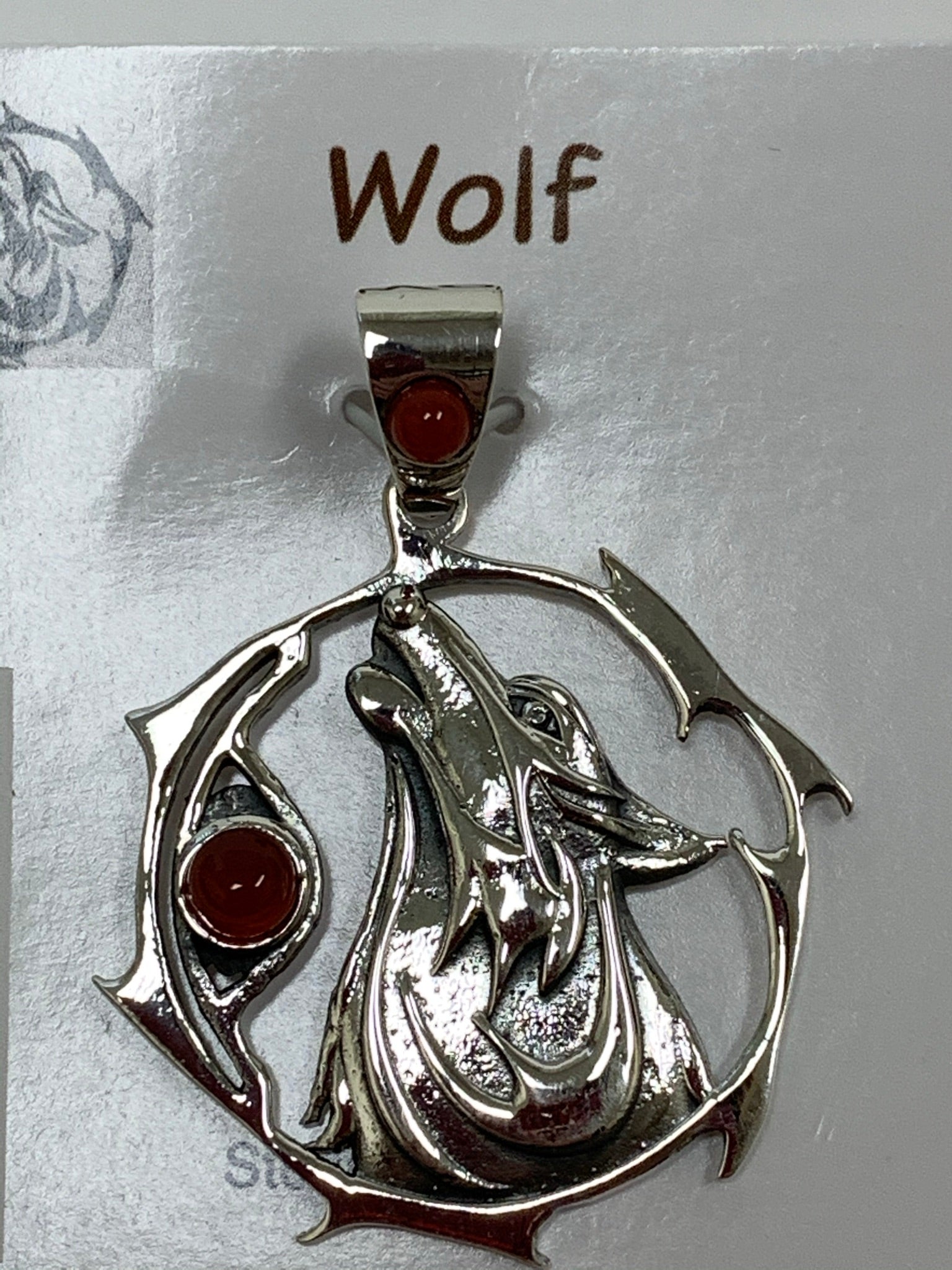 Close-up view of the sterling Silver wolf spirit animal pendant. Howling wolf (head and part of body) inside a fancy, stylized circle. Two red onyx gemstones (cabs), one on the actual pendant and one on the bail. Wear your spirit animal on your chest and carry it with you wherever you go! (Pendant only, no necklace chain).