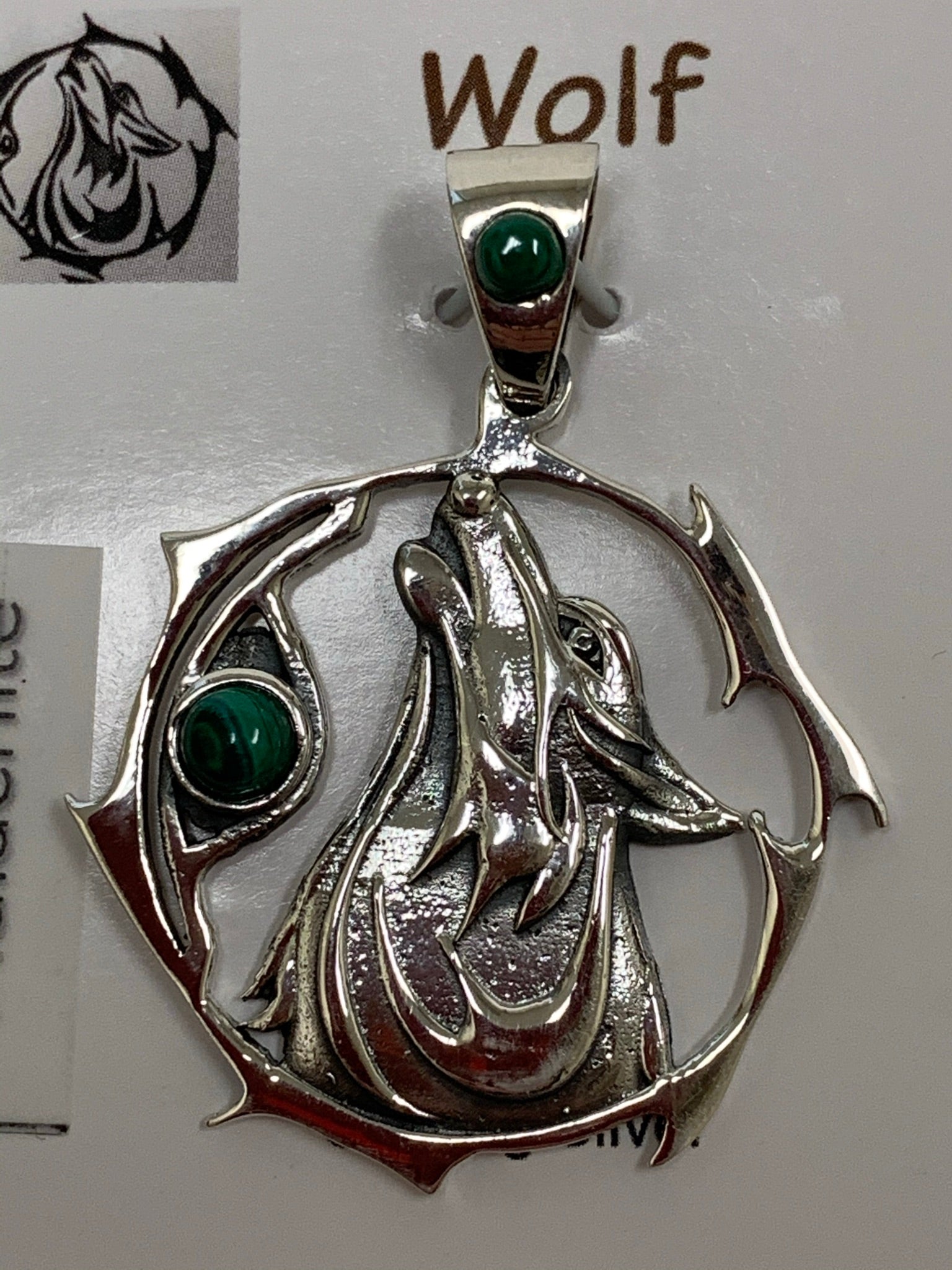 Close-up view of sterling Silver wolf spirit animal pendant. Howling wolf (head and part of body) inside a fancy, stylized circle. Two malachite gemstones (cabs), one on the actual pendant and one on the bail. Wear your spirit animal on your chest and carry it with you wherever you go! (Pendant only, no necklace chain).