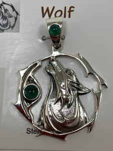 Close-up view of the sterling silver wolf spirit animal pendant. The sterling silver wolf is howling and consists of the head, neck and part of the body. It is inside of a stylized sterling circle and has two green onyx gemstones (cabs), one on the actual pendant, beside the wolf, and one on the pendant's bail. Wear this wolf symbol on your chest and carry its energy wherever you go. This is a pendant only - there is not a necklace chain included.