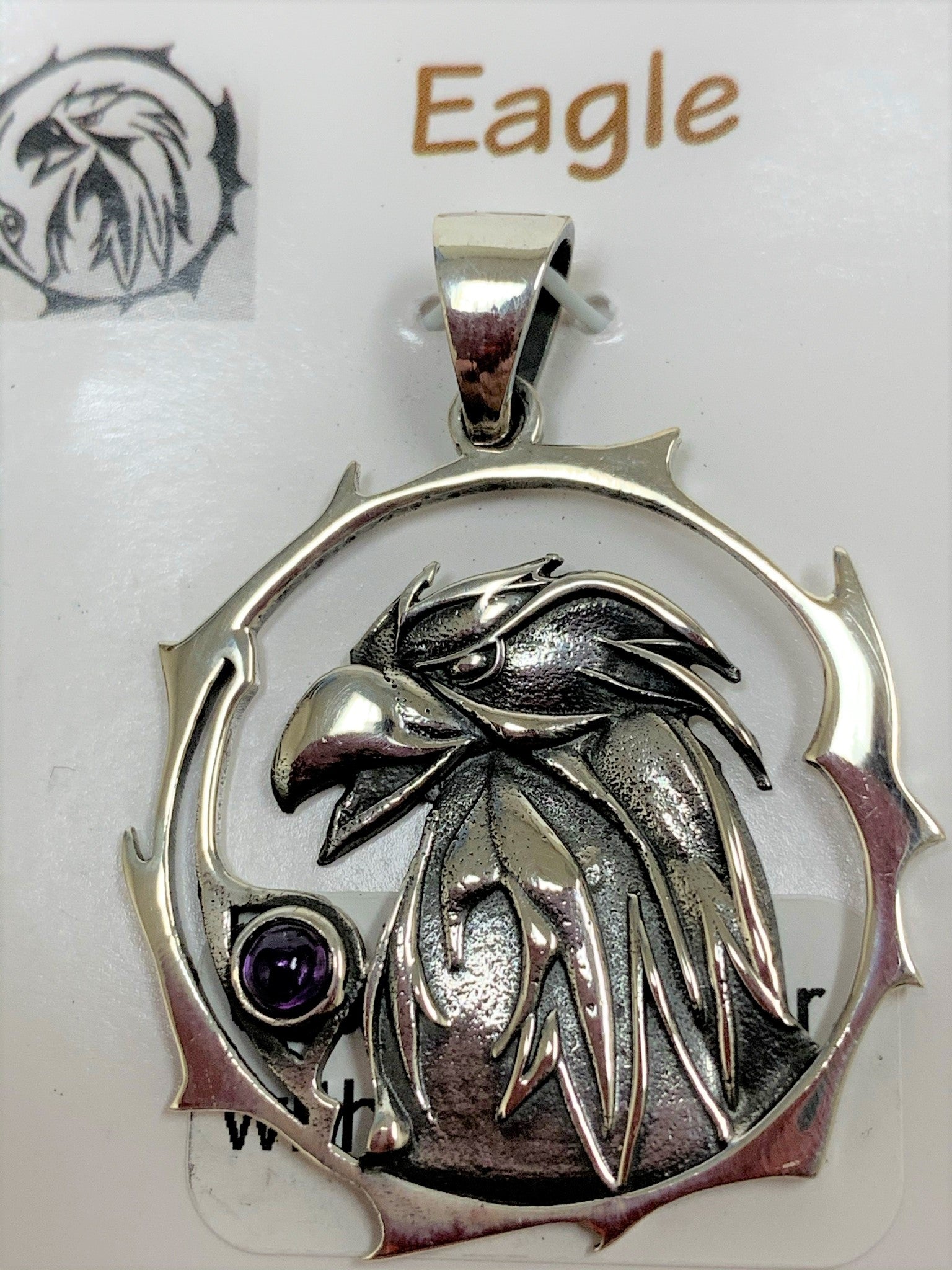 Close-up view. Sterling silver eagle animal spirit pendant, accented with an amethyst gemstone. Eagle (head and neck) is set within an open, stylized circle with the amethyst along the side (eagle and circle are sterling). Wear your spirit animal's energy so you can have it everywhere you go. Pendant only - necklace chain not included.