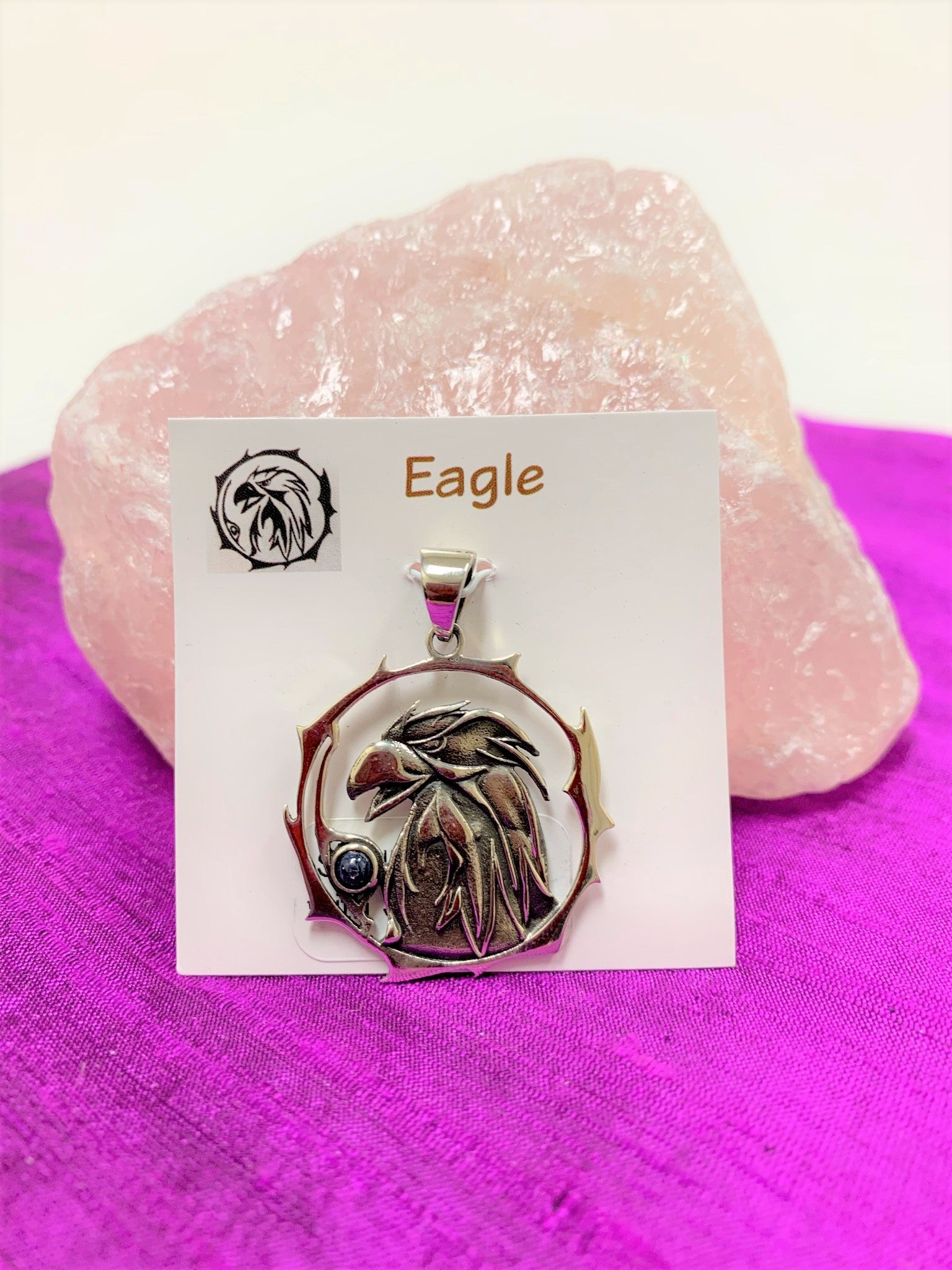 Sterling silver eagle animal spirit pendant, accented with a blue sapphire gemstone. The eagle (head and neck) is set within an open, stylized circle with the gemstone on the lower side (eagle and circle are sterling). Wear your spirit animal so you will have its energy with you wherever you go! Pendant only - necklace chain not included. 