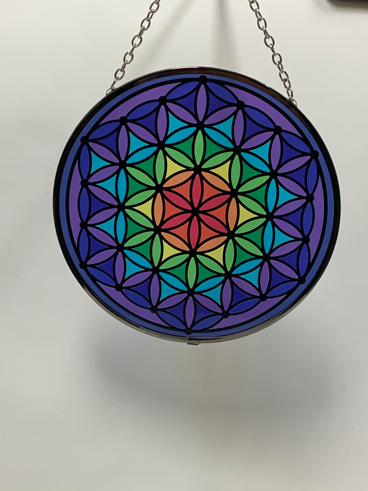 Round, glass flower of life suncatcher in the colors of the rainbow moving from the center (red) to the edge (purple). The already vibrant color is enhanced when the sun's rays stream through it. Beauty and spiritual meaning - nice combo! Comes with a chain for hanging and a suction cup, with a hook,  to hold it.