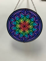 Load image into Gallery viewer, Round, glass flower of life suncatcher in the colors of the rainbow moving from the center (red) to the edge (purple). The already vibrant color is enhanced when the sun&#39;s rays stream through it. Beauty and spiritual meaning - nice combo! Comes with a chain for hanging and a suction cup, with a hook,  to hold it.

