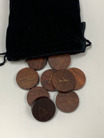 Load image into Gallery viewer, Close-up view of the wooden rune set with symbols in brass. Set comes with a velvet, drawstring bag for storing the runes. Each rune is approximately 1½&quot; in diameter and approximately ½&quot; thick. Originally, most runes were made out of wood. Comes with paper instruction sheet.
