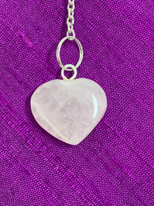 Close-up view of the rose quartz heart at the end of the pendulum's chain.
