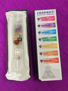 This is the clear quartz pendulum shown in its white satin-lined box that has information printed on it revealing the names of the 7 gemstone chakra beads and the name and associated color of each of the chakras