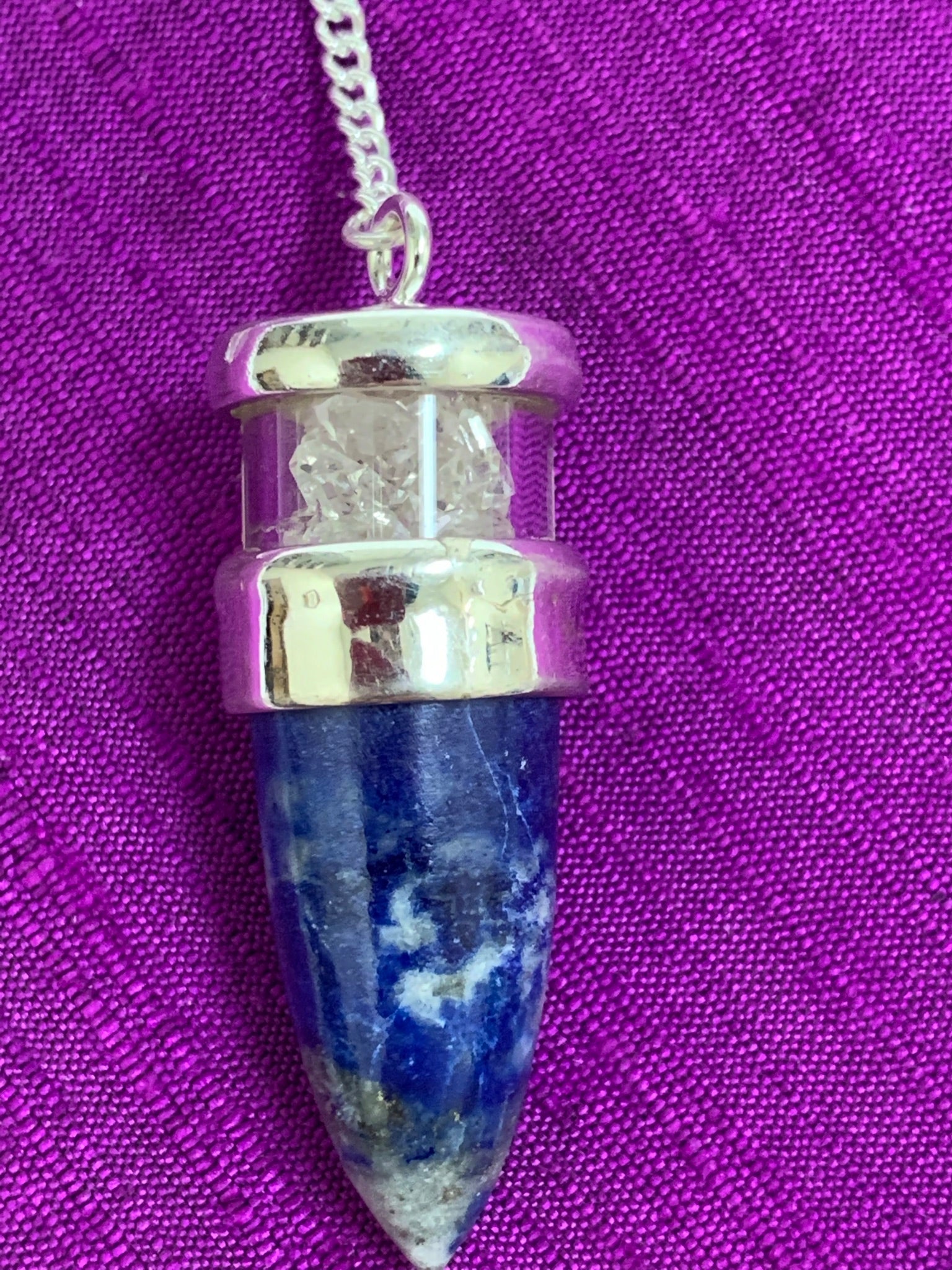 Close-up view. Elegant pendulum with lapis gemstone set in sterling silver with Herkimer diamond chips above it, encased in glass and a clear quartz bead at the opposite end of the silver chain. Pendulums are used as divination tools for receiving information from your guides, angels and higher Self.