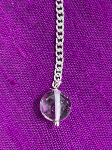 Close-up view of the clear quartz gemstone bead at the end of the pendulum chain.