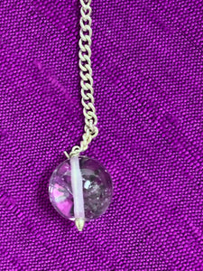 Close-up view of the clear quartz gemstone bead at the end of the pendulum chain.
