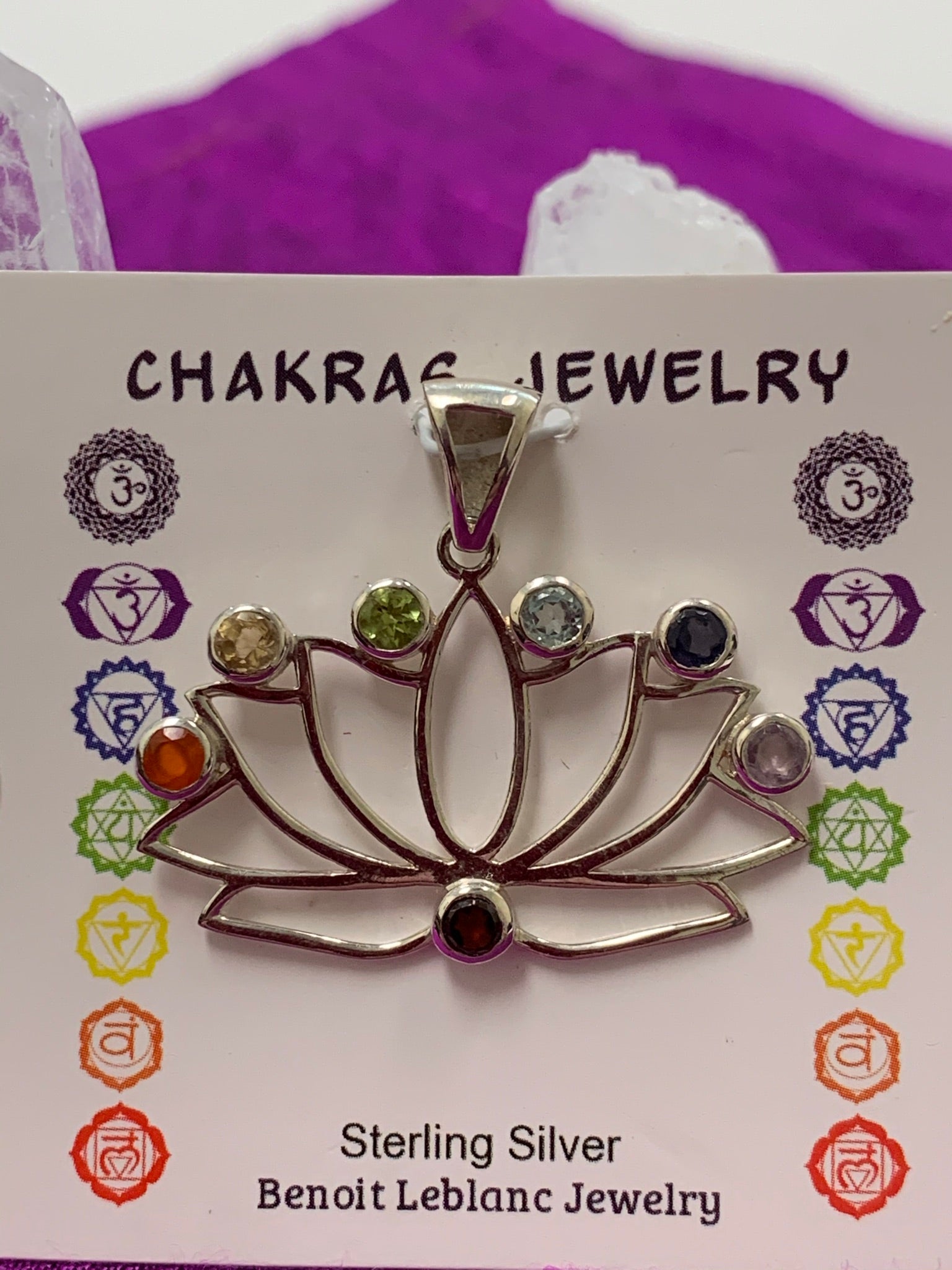 Close-up view. Open sterling silver lotus pendant with small, faceted chakra stones (one representing each of the 7 major chakras) set above the petals, with one at the bottom of the lotus (representing the root chakra). The lotus represents purity, strength and enlightenment. It also reminds us that we all have to move through the muck to reach the light. Perfect for wearing to take advantage of its benefits all day long. Approximately 1¼".