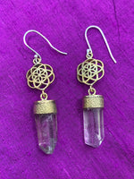 Load image into Gallery viewer, Close-up view. These crystal seed earrings are handmade in fair trade workshops (where workers are paid living wages). Raw clear quartz crystals are set into hand-cast, hypoallergenic brass. the crystals hang below a brass seed of life design. The ear wires are sterling silver. The seed of life is a universal symbol for creation and much more. Because of the handcrafting and use of raw crystals, the crystals will have slight differences within and between the pairs. Size is approximately 3&quot;x.5&quot;.
