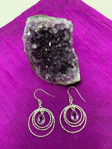 These amethyst rings of Venus earrings have three thin silver circles dangling from the ear wire. Each circle is bigger than the one before it and a faceted, tear drop amethyst hangs in the middle of the first and smallest circle. These earrings are pretty and fun! They are approximately 1¾" long. 