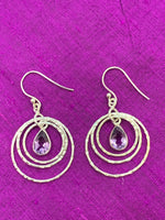 Load image into Gallery viewer, Close up view. These amethyst rings of Venus earrings have three thin silver circles dangling from the ear wire. Each circle is bigger than the one before it and a faceted, tear drop amethyst hangs in the middle of the first and smallest circle. These earrings are pretty and fun! They are approximately 1¾&quot; long.
