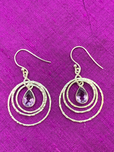 Close up view. These amethyst rings of Venus earrings have three thin silver circles dangling from the ear wire. Each circle is bigger than the one before it and a faceted, tear drop amethyst hangs in the middle of the first and smallest circle. These earrings are pretty and fun! They are approximately 1¾" long.