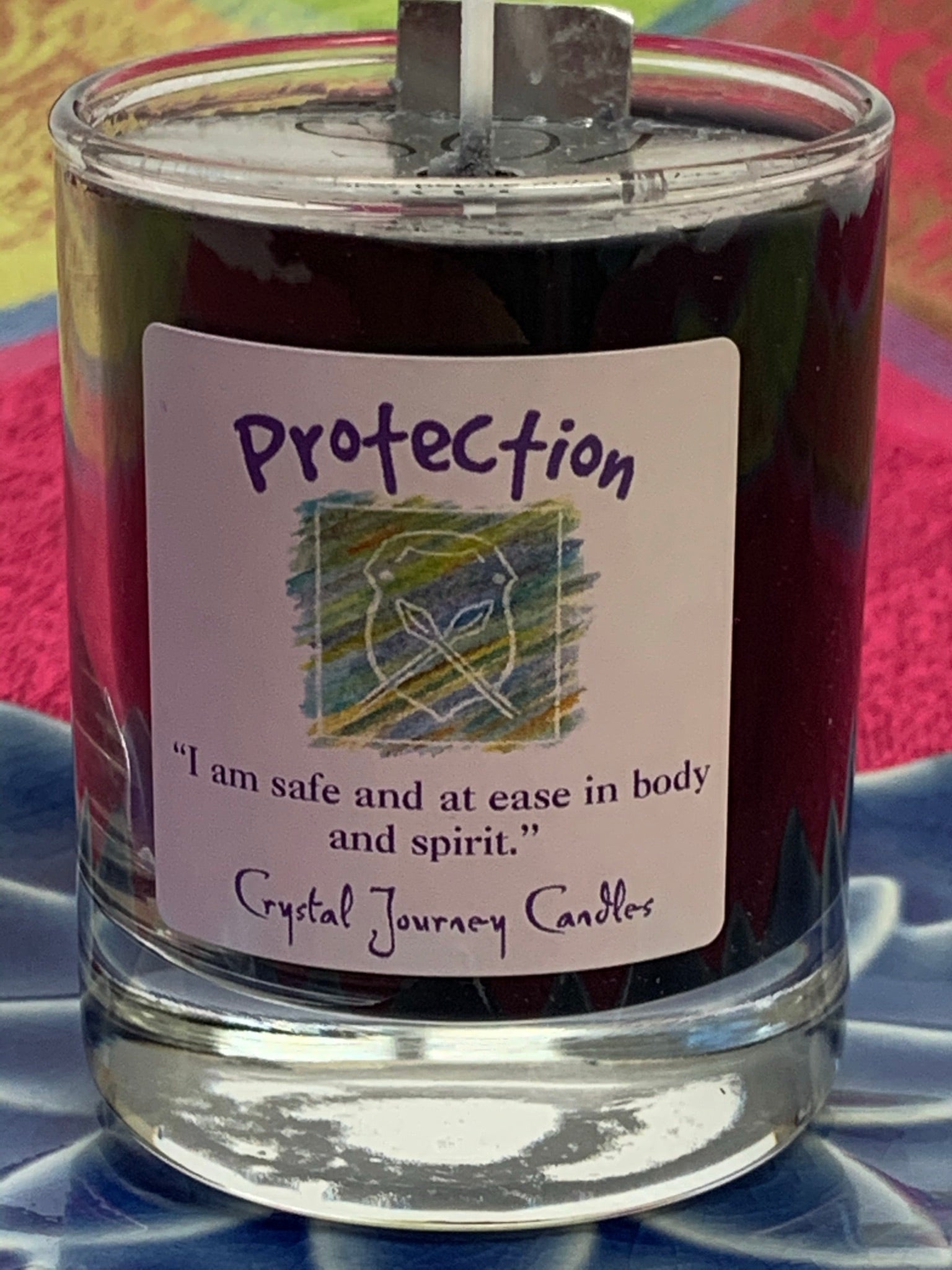 Close-up view of the handcrafted black votive candle a in glass holder. The wax is soy-based (no paraffin) and it is also vegan. Wicks are made with paper and cotton only. This candle is for "protection" and an associated affirmation is printed on the label for your use - "I am safe and at ease in body and spirit."