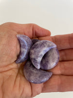 Load image into Gallery viewer, View of several lepidolite crescent moons. This sparkly little lavender colored lepidolite crescent moon can be used for meditation, healing, for your altar, on/near your computer or as décor for any room in your home or office. Easy to slip right into your pocket so you can take the energy of lepidolite everywhere you go. Approx. 1¼&quot;. Cost is $6 for one moon.
