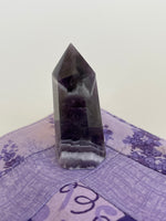 Load image into Gallery viewer, Alternate view. Chevron amethyst tower with the coolest banding for your altar, for healing or as décor for any room in your home or office. Amethyst, one of the most spiritual gemstones, heals, cleanses &amp; calms, allowing you to reach meditative &amp; higher consciousness levels more easily. It also helps to dispel negative emotional states and more. Chevron amethyst is a combination of amethyst and white quartz and when you add the quartz you get additional qualities. 2&quot; long. Cost is $9.
