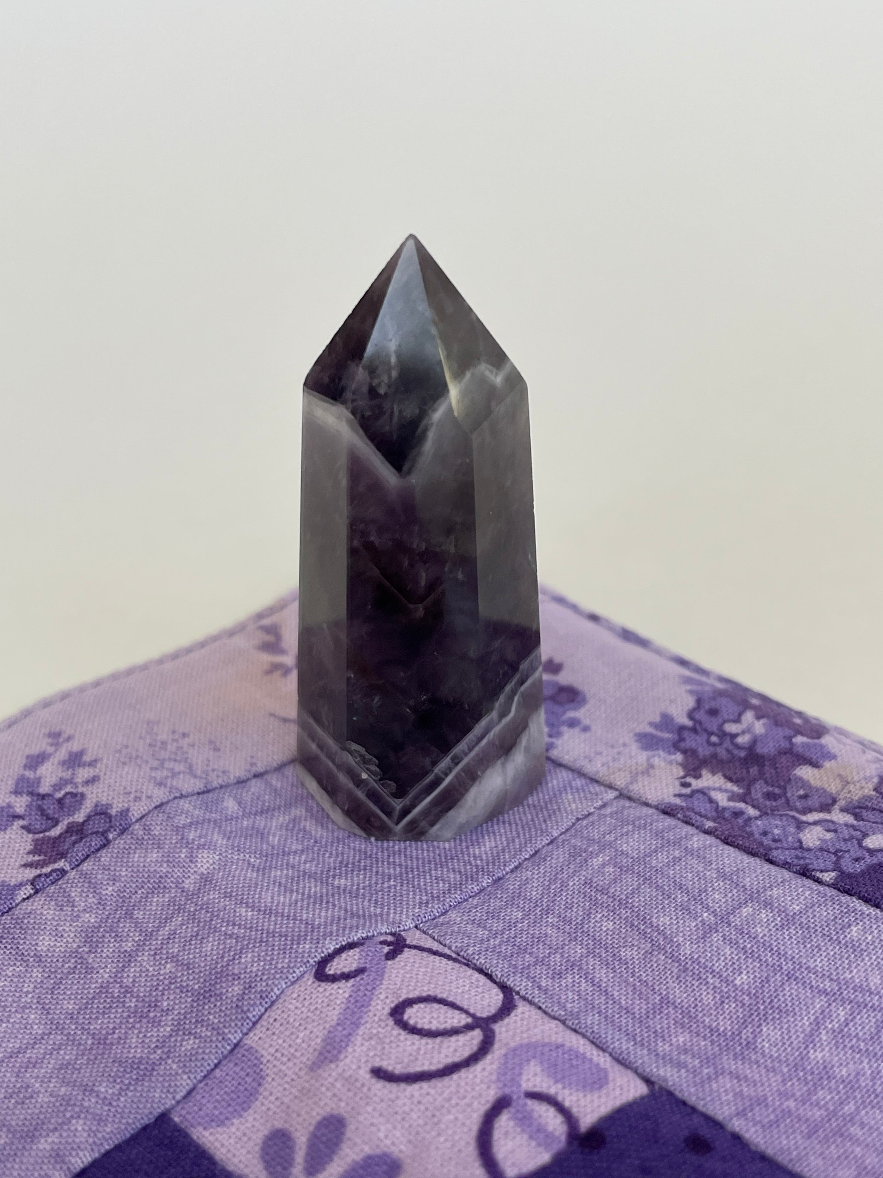 Alternate view. Chevron amethyst tower with the coolest banding for your altar, for healing or as décor for any room in your home or office. Amethyst, one of the most spiritual gemstones, heals, cleanses & calms, allowing you to reach meditative & higher consciousness levels more easily. It also helps to dispel negative emotional states and more. Chevron amethyst is a combination of amethyst and white quartz and when you add the quartz you get additional qualities. 2" long. Cost is $9.