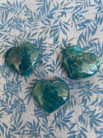 Load image into Gallery viewer, View of several hearts. Love this blue apatite heart! Great to carry in your pocket, place on your altar or bookshelf or to hold during meditation. Apatite enhances manifestation, aids psychic abilities and meditation, helps you to express yourself verbally, aids in reaching high levels of spiritual guidance, boosts creativity and helps to ease anger and irritation (along with other wonderful qualities). The apatite heart is approximately 1¼&quot; at it&#39;s widest/longest expanse. Cost is $6
