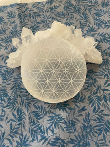 Alternate view. Beautiful selenite full moon charging plate, etched with the flower of life, can be used for cleansing and charging your crystals and jewelry because it dispels negative and unwanted energies. Selenite also promotes clarity of mind, opens the crown chakra, helps to access angelic energies and guidance from the higher realms. It brings peace and is a great stone to use while meditating or connecting spiritually and more. Approx. 3". Cost is $10.