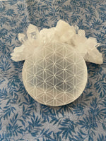 Load image into Gallery viewer, Alternate view. Beautiful selenite full moon charging plate, etched with the flower of life, can be used for cleansing and charging your crystals and jewelry because it dispels negative and unwanted energies. Selenite also promotes clarity of mind, opens the crown chakra, helps to access angelic energies and guidance from the higher realms. It brings peace and is a great stone to use while meditating or connecting spiritually and more. Approx. 3&quot;. Cost is $10.
