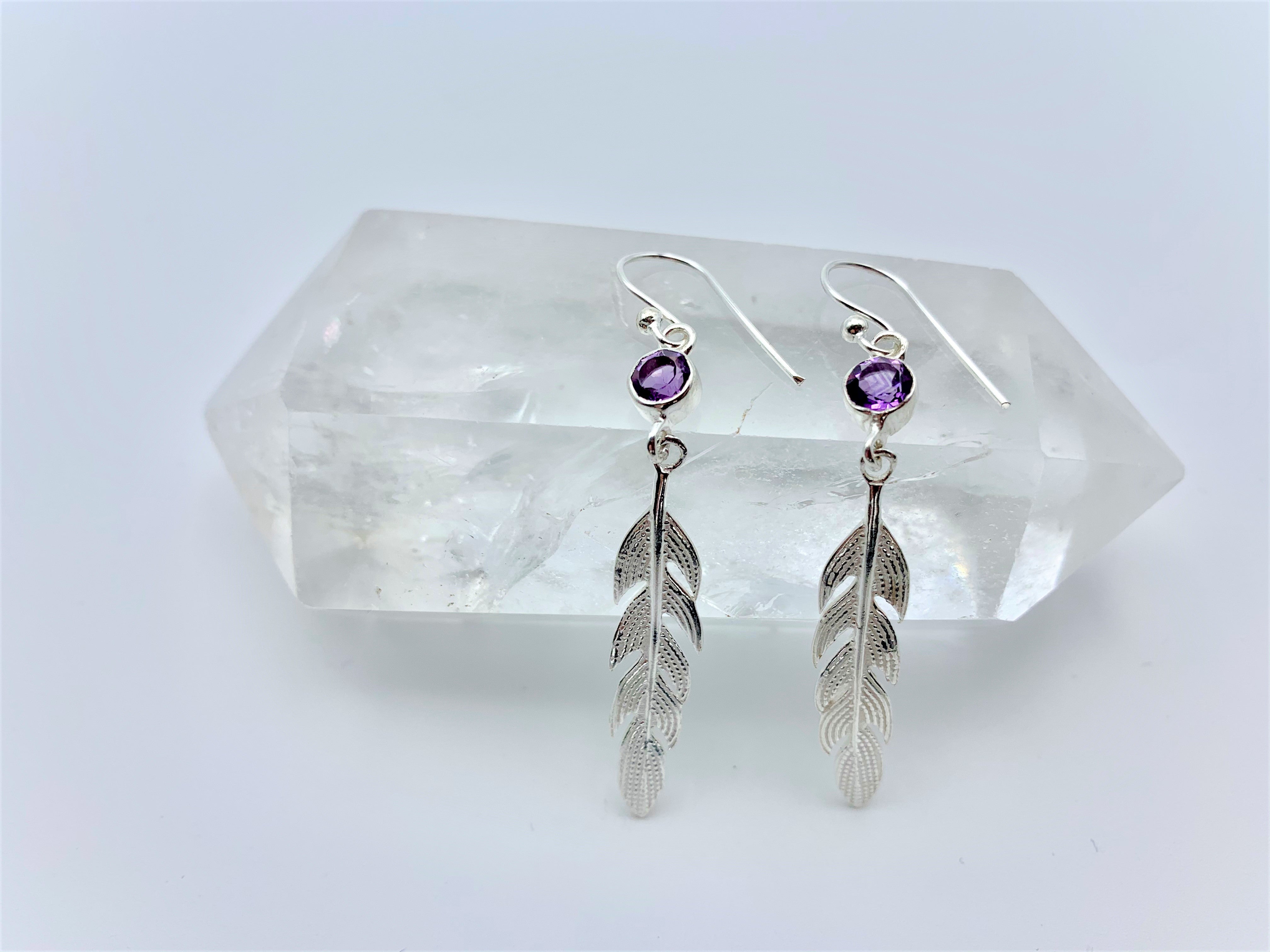 Round faceted amethyst gemstones are set in sterling silver (one in each earring) with long sterling feathers dangling below them. These have wires, not posts and are approximately 2" long.