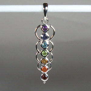 Close-up view. Chakra energy link pendant. Small faceted stones that represent each of the chakras: amethyst/crown, iolite/third eye, blue topaz/throat, peridot/heart, citrine/solar plexus, carnelian/sacral (or naval), garnet/root (or base). These stones, set in links or loops of sterling silver, two per loop or link, go straight down the middle. Pendant is approximately 1¾".