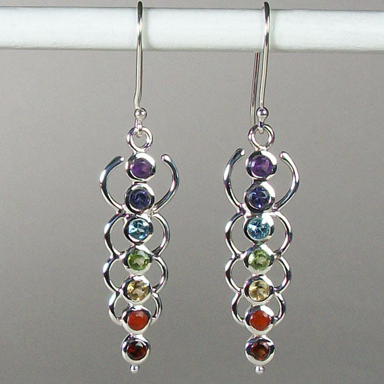 Close-up view. Chakra energy link earrings. Small faceted stones that represent each of the chakras: amethyst/crown, iolite/third eye, blue topaz/throat, peridot/heart, citrine/solar plexus, carnelian/sacral (or naval), garnet/root (or base). These stones are set in links or loops of sterling silver, two per loop or link go straight down the middle. Wires not posts and approximately 1¾".