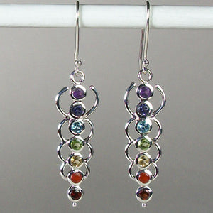 Close-up view. Chakra energy link earrings. Small faceted stones that represent each of the chakras: amethyst/crown, iolite/third eye, blue topaz/throat, peridot/heart, citrine/solar plexus, carnelian/sacral (or naval), garnet/root (or base). These stones are set in links or loops of sterling silver, two per loop or link go straight down the middle. Wires not posts and approximately 1¾".